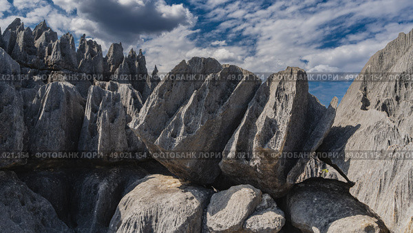 The unique karst cliffs of Madagascar. Close-up on a background of blue sky and clouds. Steep furrowed slopes, sharp peaks. Grey boulders in the foreground. Madagascar. Tsingy De Bemaraha (2023 год). Стоковое фото, фотограф Вера Ивановна Кубарева / Фотобанк Лори