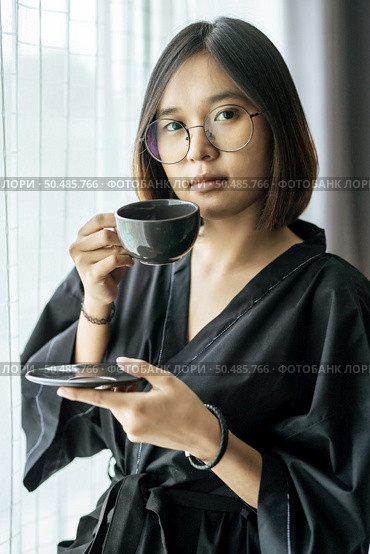 The woman wore a black robe near the window and drank coffee in the bedroom. Стоковое фото, агентство Ingram Publishing / Фотобанк Лори