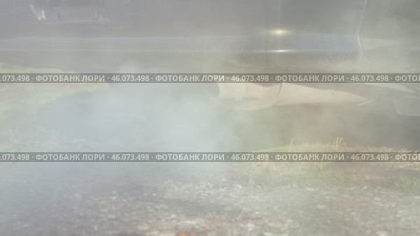 Thick plumes of exhaust smoke billow from the tailpipe of a vehicle, shrouding the surrounding natural landscape in an obscuring haze. Slow motion. An old car is poisoning the air. Стоковое видео, видеограф Воловодов Владимир / Фотобанк Лори