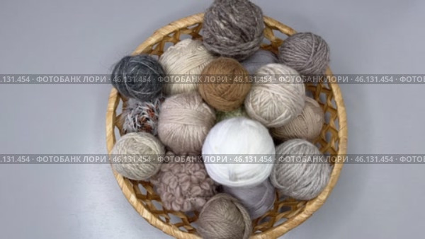 Time-lapse video of balls of beige colors wool knitting and crochet yarn being placed in wicker basket on table. Crochet hooks and knitting needles nearby. View from above, close-up, sped up. Стоковое видео, видеограф Виктория Катьянова / Фотобанк Лори