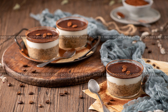 Tiramisu chia puddings elegantly served in glass cups, topped with cocoa powder and coffee beans, styled with a rustic wooden table and soft fabric. Стоковое фото, агентство Ingram Publishing / Фотобанк Лори