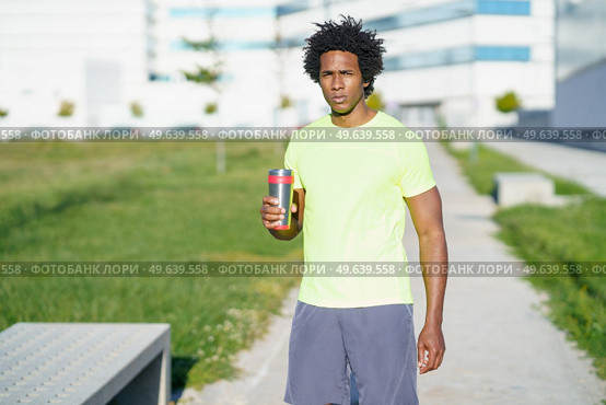 Tired African American male athlete standing with cup of water in street and having break during training in summer while looking at camera. Tired African American sportsman with water in city. Стоковое фото, агентство Ingram Publishing / Фотобанк Лори