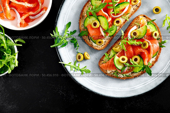 Toasts with salted salmon, arugula, green olives and cucumber, copy space, top down view. Стоковое фото, агентство Ingram Publishing / Фотобанк Лори