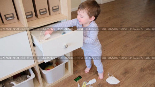 Toddler baby opened the cabinet drawer with pills and medicine. Child boy holding a pack of pills in the home living room. Kid aged about two years (age one year nine months) Стоковое видео, видеограф Андрей Журавлев / Фотобанк Лори