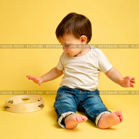 Toddler baby plays the tambourine, a child with a percussion musical instrument on a studio yellow background. Happy child musician playing hand drum. Kid aged one year four months. Стоковое фото, фотограф Андрей Журавлев / Фотобанк Лори