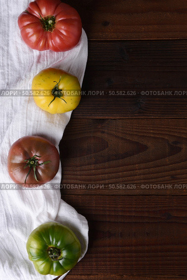 Top view of heirloom tomatoes on a kitchen towel and dark wood table. Стоковое фото, агентство Ingram Publishing / Фотобанк Лори