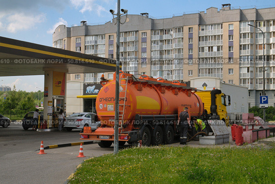 Топливовоз с горючим на городской автозаправке, рабочие осуществляют перекачку топлива в подземные резервуары на фоне жилого дома. Редакционное фото, фотограф Николай Васильев / Фотобанк Лори