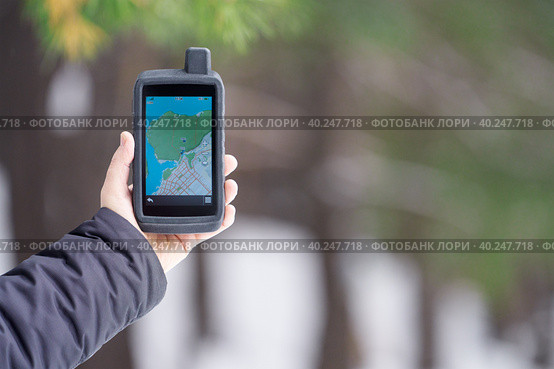 Tourist navigator in a shockproof rubberized case in a man's hand on a blurry background of a winter forest. On the screen is a map of the area and waypoints. Стоковое фото, фотограф Роман Дзюбало / Фотобанк Лори