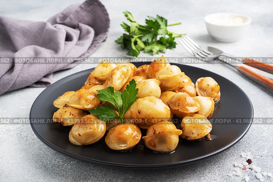 Traditional fried pelmeni, ravioli, dumplings filled with meat on black plate, russian kitchen. Gray concrete background, copy space. Стоковое фото, фотограф Глущенко Елена / Фотобанк Лори