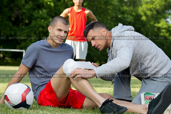 trainer bandaging athletes knee injury. Стоковое фото, агентство Ingram Publishing / Фотобанк Лори