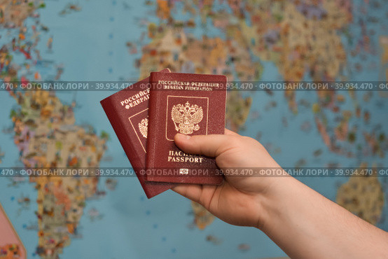 Travelling with a Russian passport around the world: two Russian sports are holding in their hands against the backdrop of the map of the world. Путешествие с паспортом Российской Федерации : в руке держит два росссийских загранпаспорта на фоне карты мира. Стоковое фото, фотограф Тамара Сахарова / Фотобанк Лори