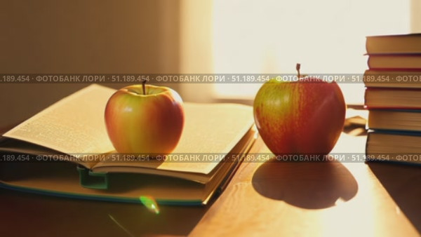 Two apples sit on an open book placed on a wooden table, while warm sunlight streams through the window, creating a cozy atmosphere in the study. Стоковое AI-видео, аниматор Данила Большаков / Фотобанк Лори