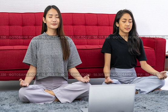 Two asian Woman do meditate from online meditation coaching to relax and reduce stress and strain for good mental health cause from city lockdown from coronavirus COVID-19 Pandemic. Стоковое фото, агентство Ingram Publishing / Фотобанк Лори