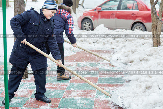 Two boys clean artificial green-red covering of playground with snow shovels. Стоковое фото, фотограф Losevsky Pavel / Фотобанк Лори