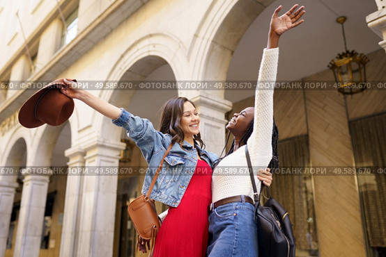Two friends happy to see each other on the street hugging. Multiethnic women.. Two friends happy to see each other on the street hugging. Стоковое фото, агентство Ingram Publishing / Фотобанк Лори