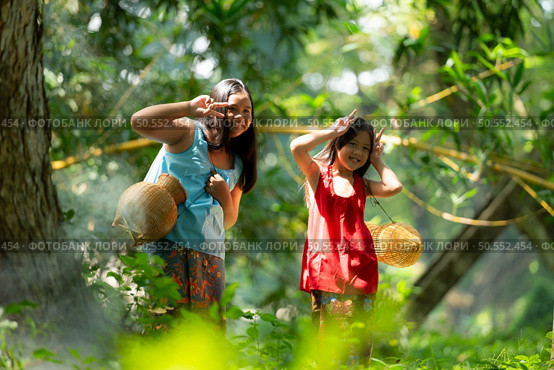 Two girls Asian women with traditional clothing stand in the rainforest. They had fun playing together before assisting Grandpa in catching fish in a nearby lake. Стоковое фото, агентство Ingram Publishing / Фотобанк Лори