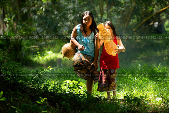 Two girls Asian women with traditional clothing stand in the rainforest. They had fun playing together before assisting Grandpa in catching fish in a nearby lake. Стоковое фото, агентство Ingram Publishing / Фотобанк Лори