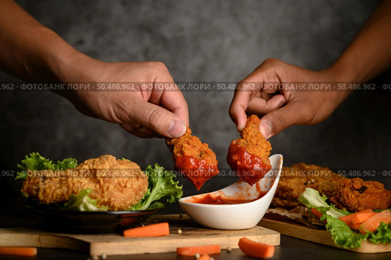 Two hand holding crispy fried chicken dipped in tomato sauce.Selective focus. Стоковое фото, агентство Ingram Publishing / Фотобанк Лори