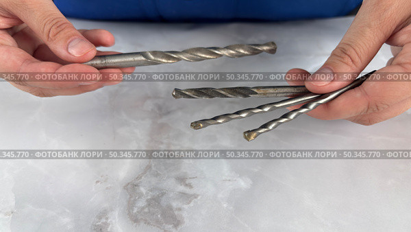 Two hands holding a selection of metal drill bits on a smooth marble surface. Стоковое фото, фотограф Анастасия / Фотобанк Лори