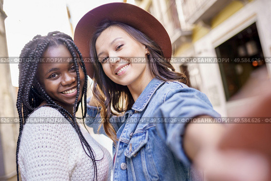 Two multiethnic women making selfie and grimacing with a smartphone.. Two beautiful multiethnic women making selfie and grimacing. Стоковое фото, агентство Ingram Publishing / Фотобанк Лори