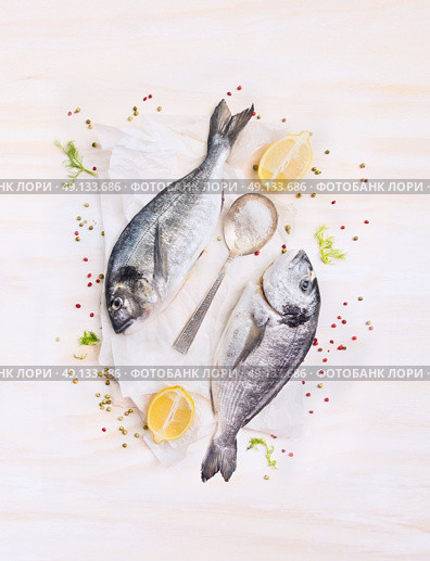 two raw dorado fish with lemon, spices and spoon on paper, composing on white wooden background, top view. Стоковое фото, агентство Ingram Publishing / Фотобанк Лори