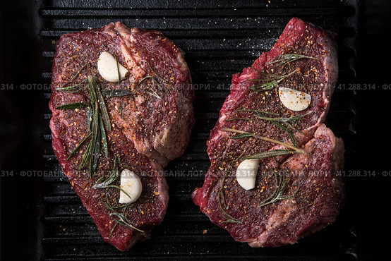 Two raw ribeye steaks with spices, rosemary and garlic on a grill pan. Стоковое фото, фотограф Максим Коломыченко / Фотобанк Лори