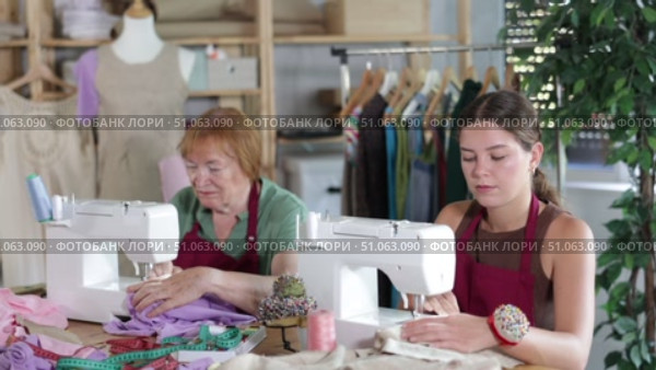 Two seamstresses work together and sew a collection of clothes on sewing machines in the workshop. Female dressmakers sitting at a table and sewing clothes to order. Стоковое видео, видеограф Яков Филимонов / Фотобанк Лори