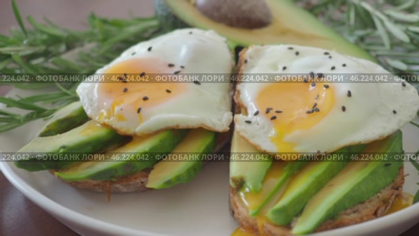 Two Toasts with avocado and fried egg Spreading Yolk, rosemary 4K. Preparing healthy toast breakfast avocado slices rye wholegrain bread, sunny side up egg on top. Healthy breakfast for two, couple. Стоковое видео, видеограф Елизавета Малкова / Фотобанк Лори