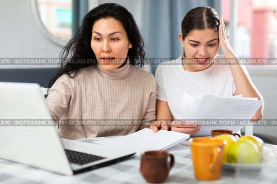 Two women with financial documents near laptop sitting at table at home. Стоковое фото, фотограф Яков Филимонов / Фотобанк Лори