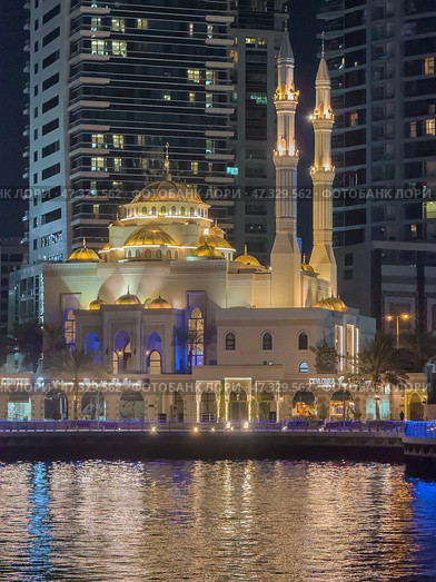 UAE, Dubai, 10 December 2024: Mosque of Muhammad Ibn Ahmad Al-Mullah against the backdrop of skyscrapers at night in Dubai Marina, yachts sailing by, reflection of night lighting on the water. Редакционное фото, фотограф Vladimir Drozdin / Фотобанк Лори