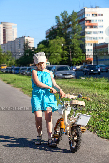 Unhappy preschool girl carrying her bicycle on asphalt lane holding steering wheel. Стоковое фото, фотограф Кекяляйнен Андрей / Фотобанк Лори