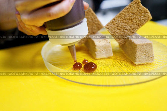 Unrecognisable chef squeezing drops of jam onto a plate of foie micuit with crunchy croutons while working in a restaurant. Crop chef plating foie micuit with crunchy croutons in restaurant. Стоковое фото, агентство Ingram Publishing / Фотобанк Лори