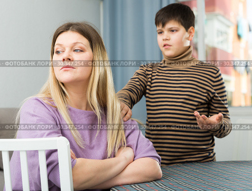Upset mother sitting at table after arguing with son indoors. Стоковое фото, фотограф Яков Филимонов / Фотобанк Лори