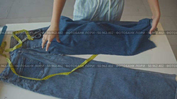 Using measuring tape, seamstress works at her table and calculates length of denim fabric she will need to work with for jeans. Стоковое видео, видеограф Strunov David / Фотобанк Лори
