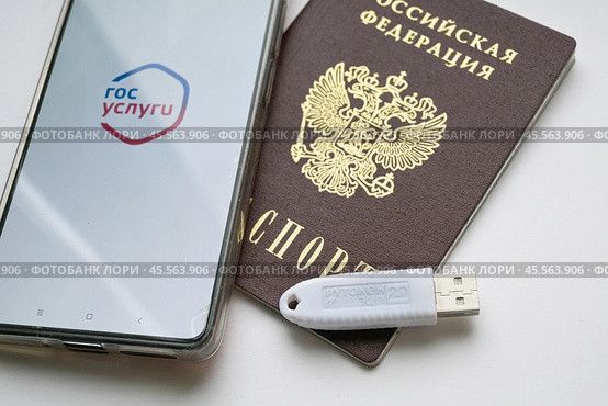 Устройство  USB eToken  (рутокен) белого цвета, устройство для хранения электронной цифровой подписи (ЭЦП) и информации для аутентификации пользователя, паспорт и телефон с приложением Госуслуги на белом фоне. Редакционное фото, фотограф Snezka / Фотобанк Лори
