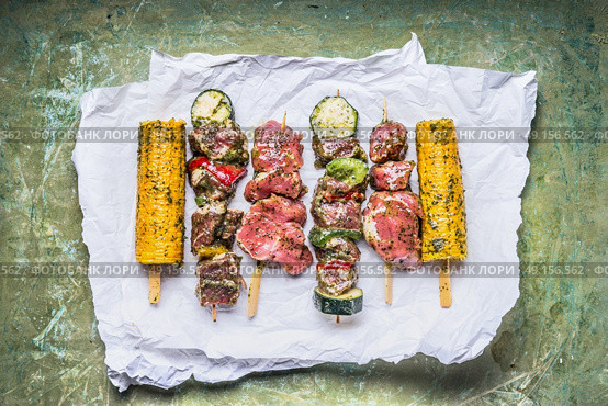 Various Meat Skewers  for grill with vegetables , corn ears and condiment on green rustic background , top view. Стоковое фото, агентство Ingram Publishing / Фотобанк Лори