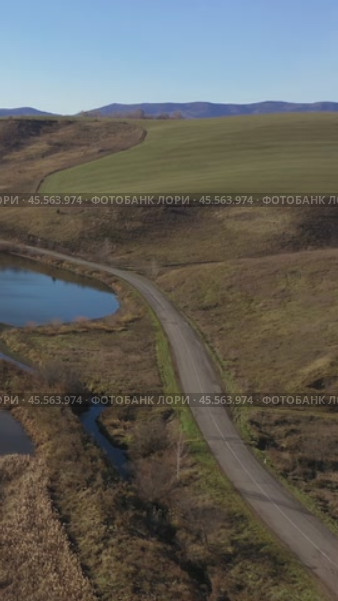 Vertical drone video of flying over a hilly rural landscape with a winding road and fish ponds. Altai Krai. Стоковое видео, видеограф Сергей Пристяжнюк (Serg Zastavkin) / Фотобанк Лори