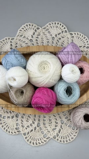 Vertical time lapse video of colorful balls of cotton yarn for hand crochet in placed by female hand in wooden plate on handmade lace napkin on light table. Wooden hooks nearby. Flat lay, close-up. Стоковое видео, видеограф Виктория Катьянова / Фотобанк Лори