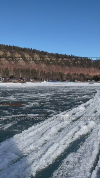 Vertical video of Siberian river Irkut in November during freeze-up on sunny day. Ice floes float on water. On shore is Shamanka village near famous Shamansky cliff, called 33 heroes bogatyrs - natural landmark. Стоковое видео, видеограф Виктория Катьянова / Фотобанк Лори