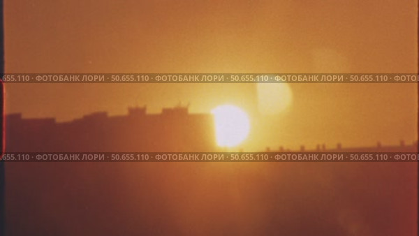 Vibrant orange sunset sinking behind darkened urban skyline, casting warm golden hues across architectural landscape with gradual chromatic transitions, 8 mm film. Стоковое видео, видеограф Данил Руденко / Фотобанк Лори