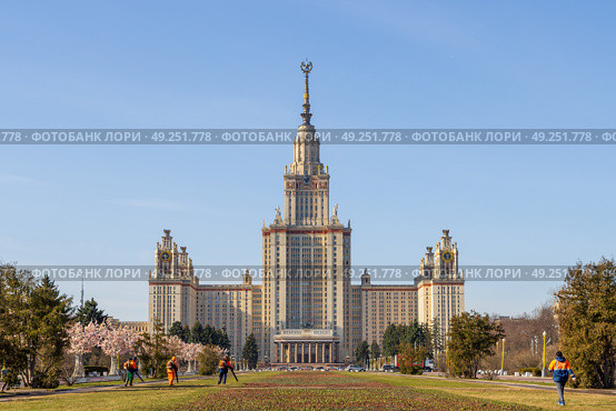 Вид на главное здание Московского государственного университета. Красивое высотное здание со шпилем. Архитектурная доминанта и достопримечательность Москвы. Дворники сдувают опавшую листву с газонов. Воробьёвы горы, Москва, Россия. (2023 год). Стоковое фото, фотограф Андрей Степанов / Фотобанк Лори