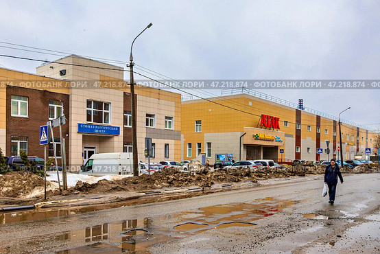Вид на разбитую автомобильную дорогу на фоне коммерческих зданий во Фрязино в дождливый пасмурный день (2024 год). Редакционное фото, фотограф Владимир Шипикин / Фотобанк Лори
