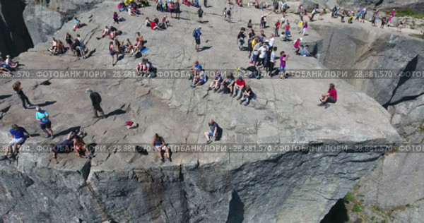 Вид на скалу Проповедника (Preikestolen) и людей, сидящих на краю. Туристическая природная достопримечательность. Норвегия (2018 год). Редакционное видео, видеограф Кекяляйнен Андрей / Фотобанк Лори