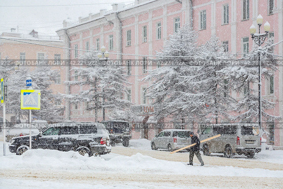 Вид на заснеженную улицу северного города. Мужчина несет доски. Припаркованные автомобили. Много снега после снегопада. Магадан, Магаданская область, Сибирь, Россия. Редакционное фото, фотограф Андрей Степанов / Фотобанк Лори