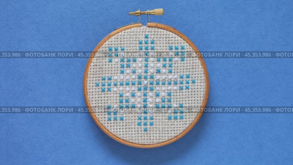 Video of hand embroidered cross stitch snowflake in wooden hoop on blue background. Winter craft, needlework and Christmas gifts concept. Cross stitches as a hobby. Flat lay, ccose-up. Стоковое видео, видеограф Виктория Катьянова / Фотобанк Лори