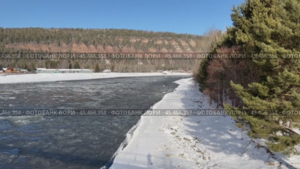 Video of Siberian river Irkut in November during freeze-up. Ice floes float on blue water. On shore is Shamanka village near famous Shamansky cliff, called 33 heroes bogatyrs - natural landmark. Стоковое видео, видеограф Виктория Катьянова / Фотобанк Лори