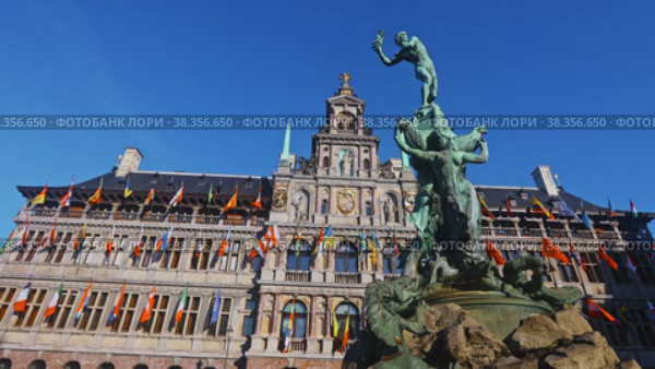 View of Brabo Fountain in front of Antwerp City Hall richly ornamented with heraldic symbols, sculptures and flags Belgium, Flanders and countries of European Union and United Nations on Grote Markt. Стоковое видео, видеограф Яков Филимонов / Фотобанк Лори