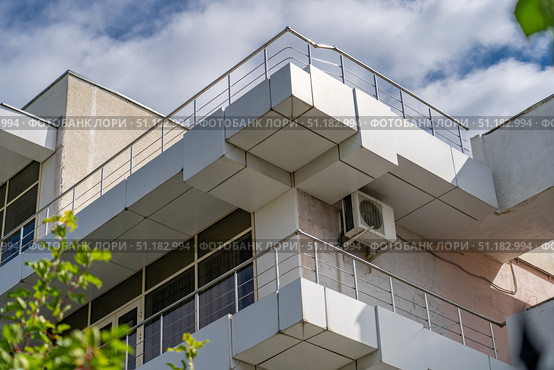 View of old building with balconies and terraces to accommodate tourists on vacation against blue sky. Bottom view of terrace of building and external air conditioning unit below it. Стоковое фото, фотограф Данила Большаков / Фотобанк Лори