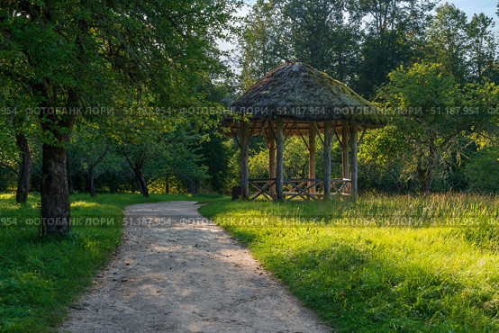 View of the ancient wooden gazebo in the apple orchard in the Mikhailovskoye Estate of the Pushkin Museum-Reserve on a sunny summer day, Pushkinskiye Gory, Pskov region, Russia. Стоковое фото, фотограф Ula Ulachka / Фотобанк Лори