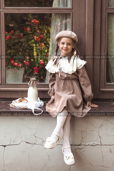 Vintage accessories and retro-style clothes. A small, beautiful girl with bows in her hair, in a beige dress and a beret outdoors with bagels and milk in a string bag. Стоковое фото, фотограф Photojuli / Фотобанк Лори
